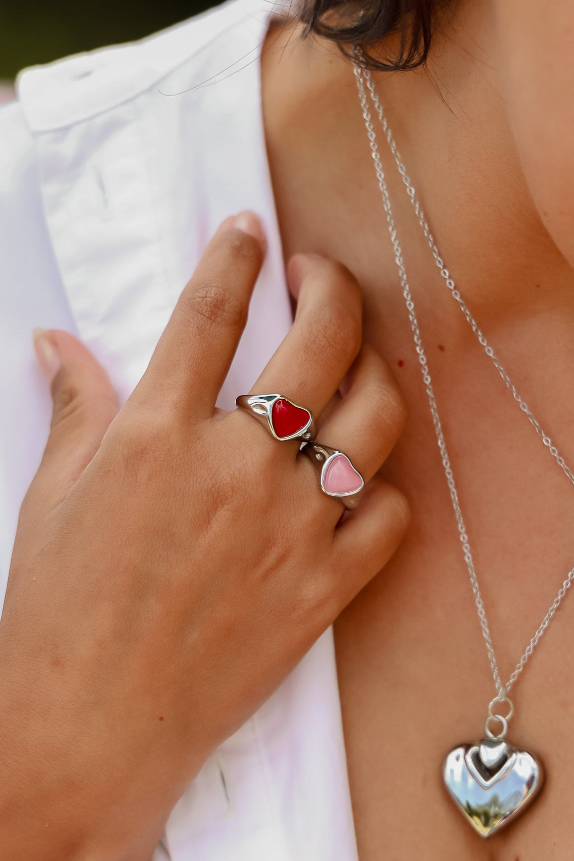 Woman wearing a silver heart-shaped necklace and earrings, with a blurred background.
