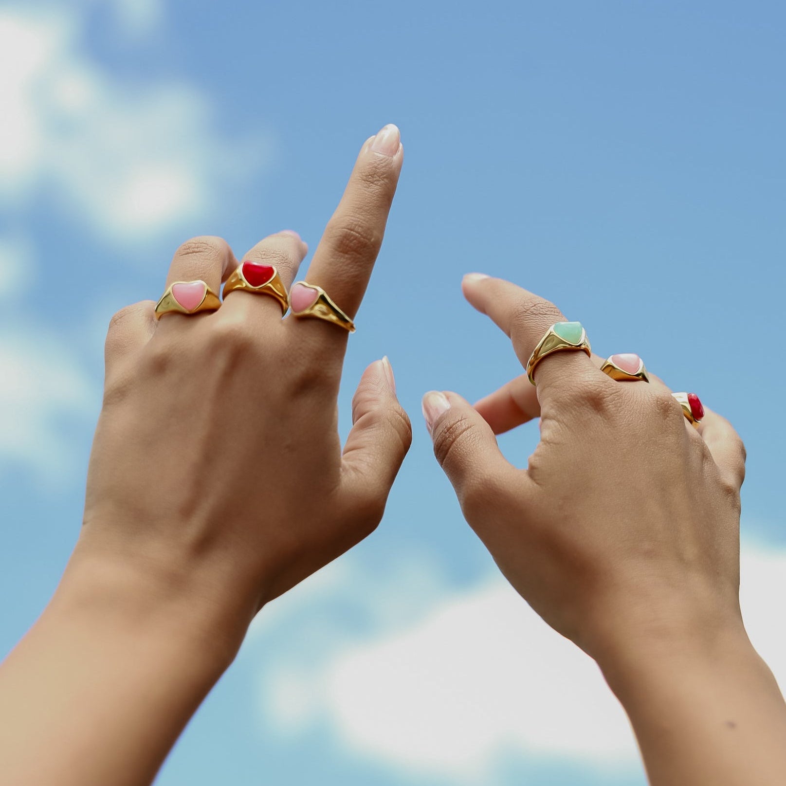 Two hands with rings pointing towards a blue sky with clouds