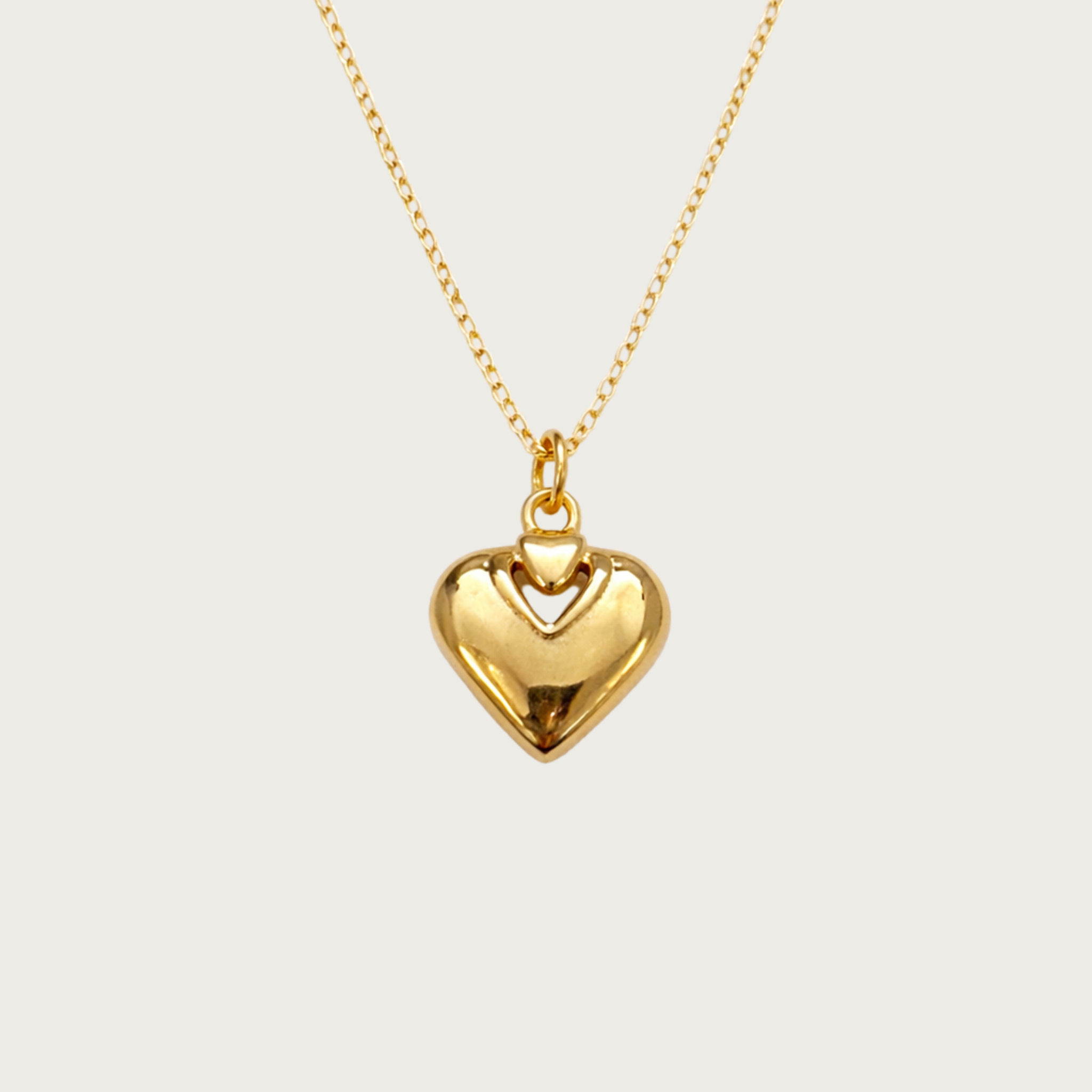 Gold heart-shaped pendant necklace on a light beige background